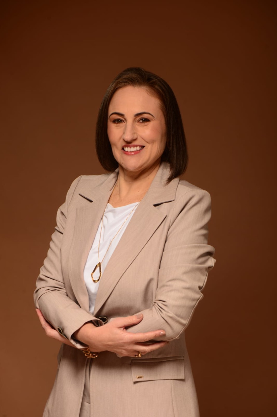 Carla Rizzi, psicóloga, de blazer claro, sorrindo de braços cruzados