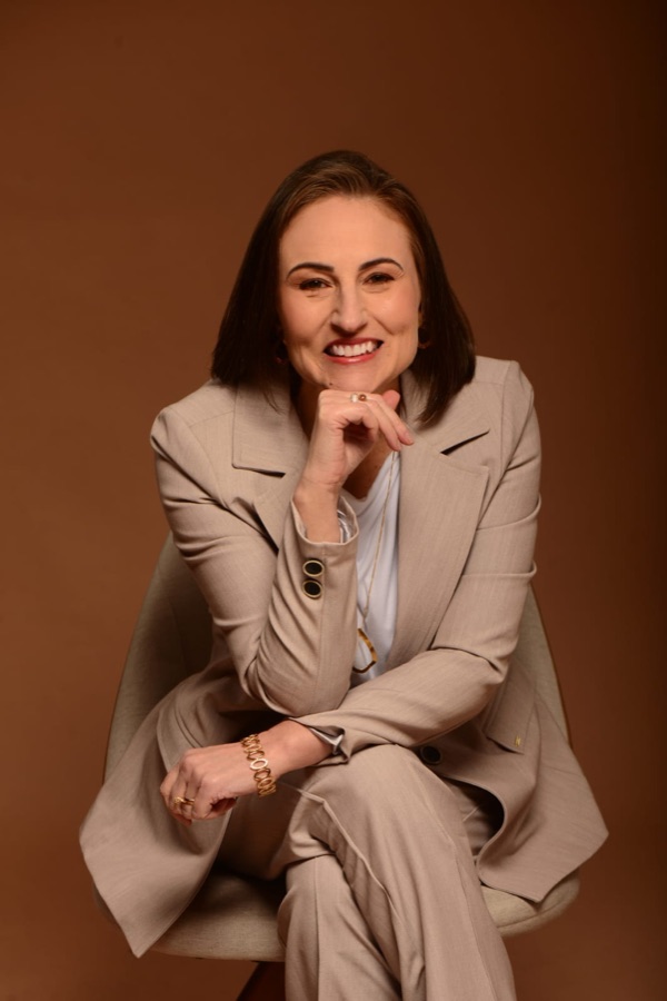 Carla Rizzi de blazer, sorrindo com a mão no queixo